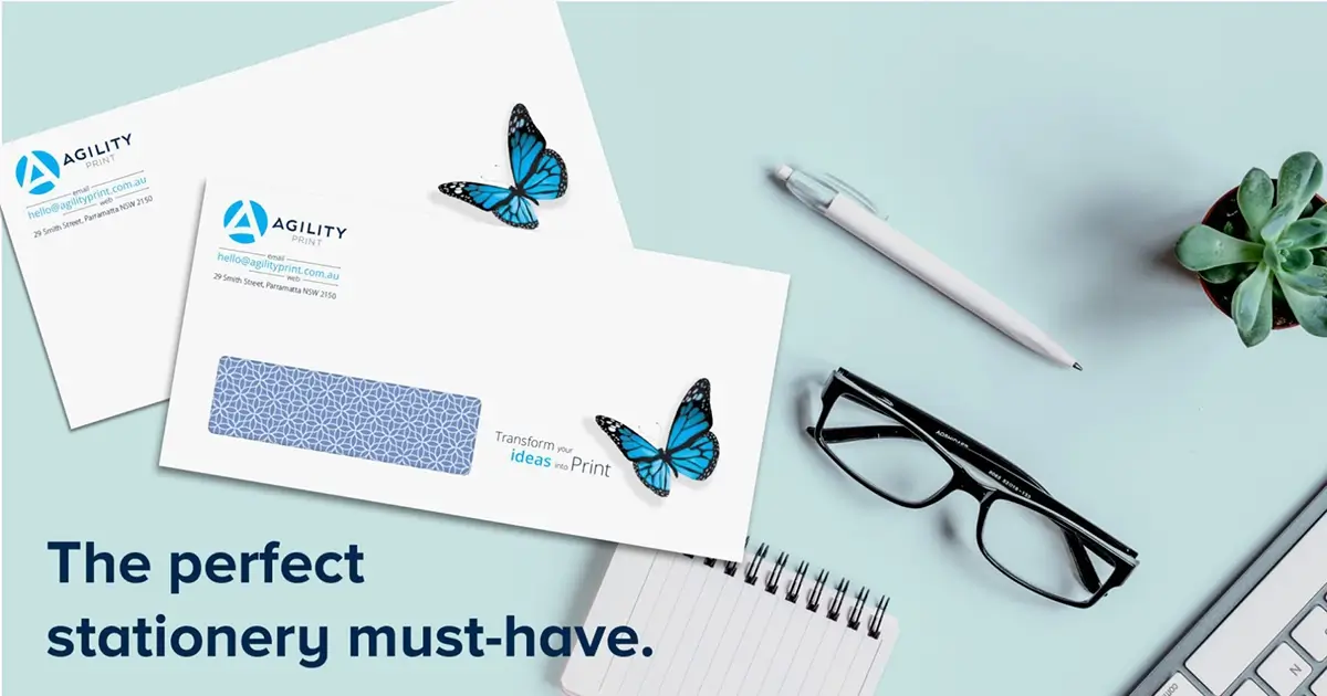 Two Agility Print branded envelopes with blue butterfly decals on a light blue desk